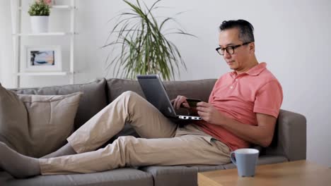 hombre-con-laptop-y-tarjeta-de-crédito-en-el-sofá-en-casa