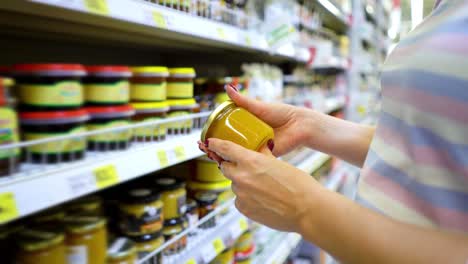 Manos-de-mujer-caucásica-de-Closeup-cerca-de-estantes-de-la-tienda-eligiendo-miel-luz-abarrotes-mercado