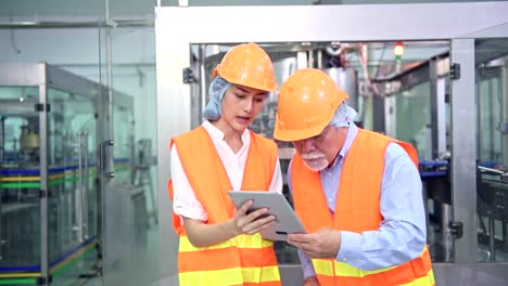 Senior-quality-inspector-teaching-junior-team-member-in-factory.-Chinese-old-male-with-his-young-team-discussing-quality-issue-with-bottle-production-line-in-background.