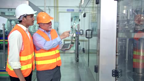 Senior-quality-inspector-teaching-junior-team-member-in-factory.-Chinese-old-male-with-his-young-team-discussing-quality-issue-with-bottle-production-line-in-background.