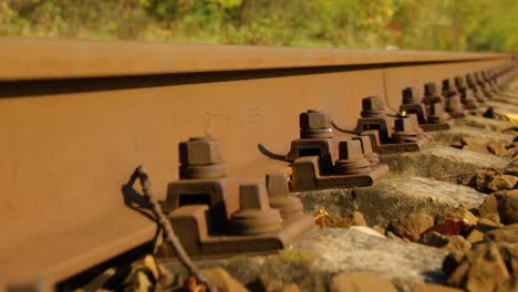 A-close-up-view-of-the-large-screws-securing-the-train-tracks-during-a-sunny-day-with-a-slow-passage-forward-with-a-turn-from-a-side-view-from-below-a-bit-above-the-stones.