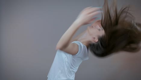 A-young-sports-model-demonstrates-her-long-hair,-I'm-in-the-studio-on-a-gray-background.-Slow-motion