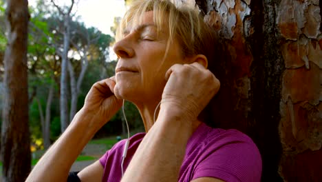 Senior-mujer-apoyado-en-un-árbol-y-escucha-música-4k