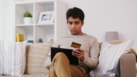 hombre-con-tablet-pc-y-tarjeta-de-crédito-en-el-sofá-en-casa