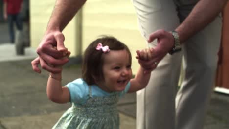 Una-feliz-niña-sonriente-camina-por-la-calle-con-la-ayuda-de-un-adulto