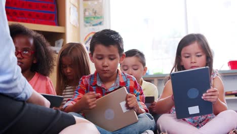 Teacher-and-pupils-sit-on-the-floor-using-tablets-in-class