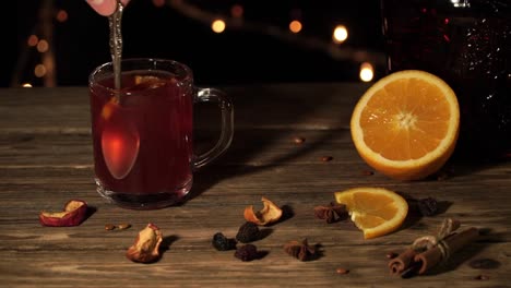 Hand-ist-Glühwein-Wein-stehen-auf-dem-Tisch-mit-Orangen-und-getrocknete-Äpfel-rühren.