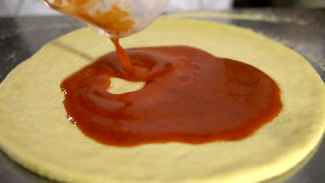 Chef-hand-is-spreading-pasteurized-tomato-paste-onto-a-Pizza-base-close-up