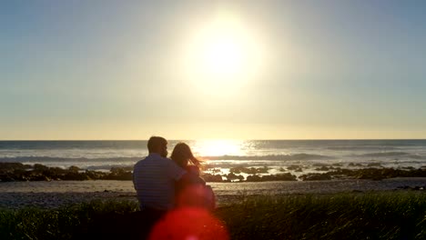 Rear-view-of-romantic-couple-sitting-at-beach-4k