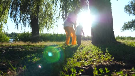 Young-father-and-little-son-holding-hands-and-walking-along-green-park-at-sunny-summer-day.-Happy-family-spending-time-together-at-nature.-Sunlight-at-background.-Low-angle-view-Slow-motion-Close-up