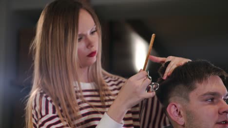 Tiro-interior-del-proceso-de-trabajo-en-peluquería-moderna.-Retrato-de-vista-lateral-de-hombre-joven-atractivo-conseguir-moda-corte-de-pelo.-Cliente-de-servicio-de-peluquería-masculina,-haciendo-corte-de-pelo-con-peine-y-tijeras-de-metal