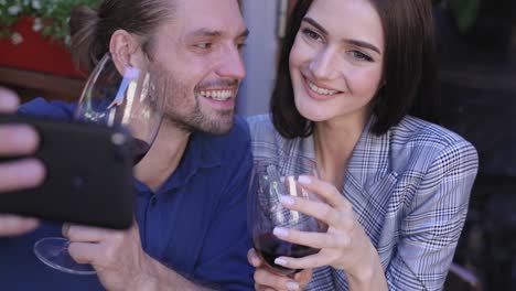 Feliz-pareja-con-vino-tomando-fotos-en-el-teléfono-en-el-restaurante