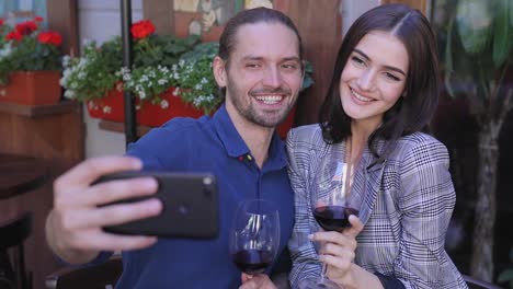 Feliz-pareja-con-vino-tomando-fotos-en-el-teléfono-en-el-restaurante