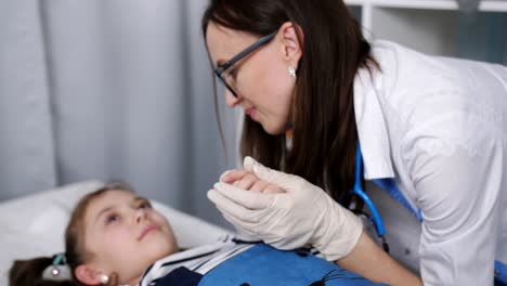 Smiling-friendly-female-doctor-talking-with-little-patient-lying-on-a-hospital-bed-in-the-pediatrician's-office