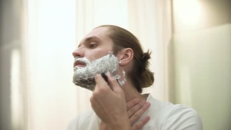 Man-Shaving-Beard-With-Razor-In-Bathroom