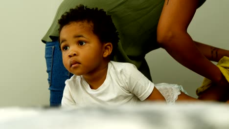 Mittelteil-der-jungen-schwarzen-Mutter-hilft-seinem-Sohn,-seine-Kleidung-auf-dem-Bett-in-bequemen-Haus-zu-wechseln-4k