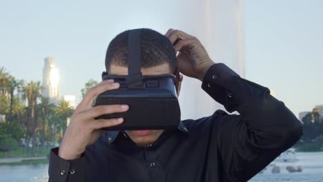 Junge-afrikanische-amerikanische-Mann-mit-VR-Brille-durch-einen-Brunnen-in-einem-Park