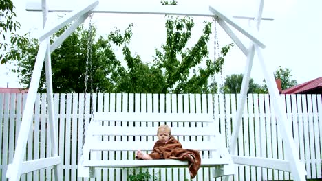 a-little-one-year-old-girl,-wrapped-in-a-towel,-with-a-dirty-face,-lonely-sitting-on-a-swing-in-the-garden,-in-the-summer.-She-has-a-sad-look.-She-wants-to-sleep