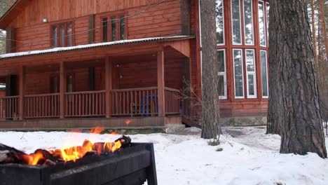 Panoramic-video-of-open-fire-in-iron-brasier-barbecue-with-cottage-on-background