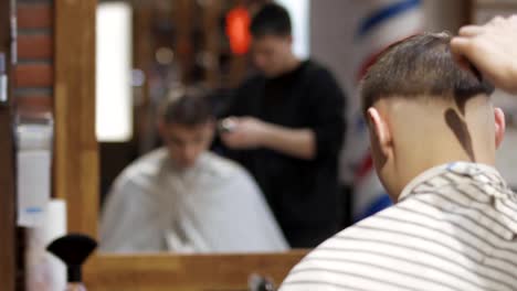 Professionelle-Friseur-schneidet-Haare-mit-elektrischen-Rasierapparat-mit-einem-jungen-Kerl