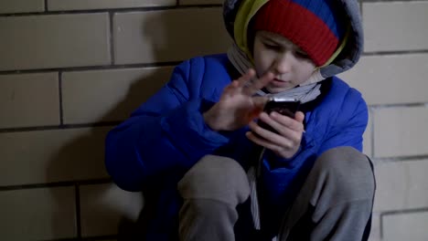 poor-boy-sits-on-the-floor-on-the-street-in-the-evening-and-uses-the-phone-in-winter