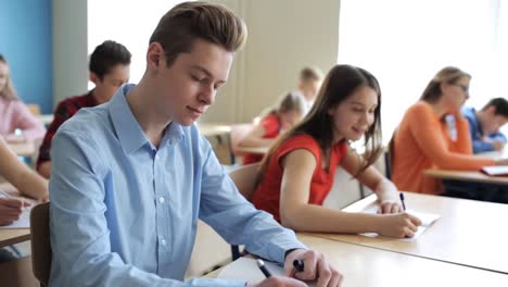 Grupo-de-estudiantes-con-cuadernos-escritura-prueba-en-la-escuela