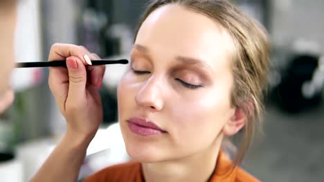 Overview-of-a-make-up-process.-Professional-make-up-artist-gently-putting-nude-eyeshadows-on-an-eyelid.-Attractive-young-blonde-model