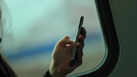 Primer-plano-de-manos-con-dispositivo-smartphone-con-paisaje-de-fondo-borroso-en-movimiento.-Persona-navegando-por-internet-y-comprobar-correo-electrónico-mientras-viaja-en-tren