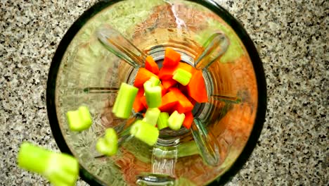 Stalk-of-an-apium-fall-on-carrots-in-a-blender-bowl.-Slow-motion.	Shooting-in-kitchen.-Top-view.