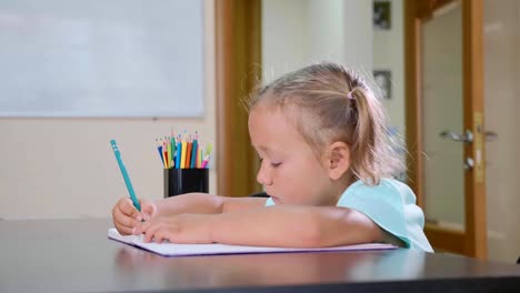 Kleine-süße-Mädchen-sitzt-im-Klassenzimmer-und-im-Heft-zu-schreiben