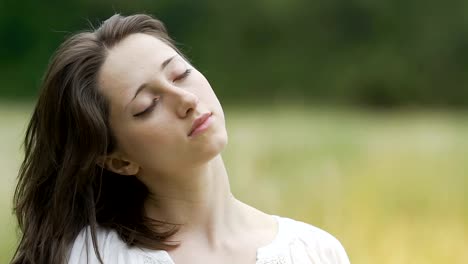 Brunette-beauty-feeling-relaxed-in-green-field-closed-eyes-combs-long-hair-hand