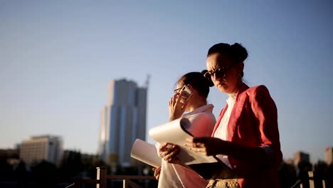 Two-women-on-the-waterfront-on-the-background-the-construction-of-tall-buildings-to-discuss-details-of-the-alleged-construction-works.