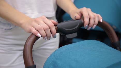 A-woman-is-holding-a-baby-carriage-by-her-hands,-close-up