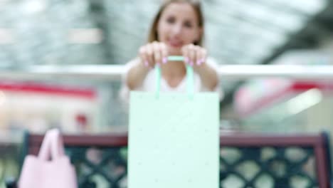 Chica-feliz-mostrando-hermoso-papel-bolsa-en-sus-manos-sentado-en-el-Banco-en-el-centro-comercial,-se-desvanecen-en-el-tiro