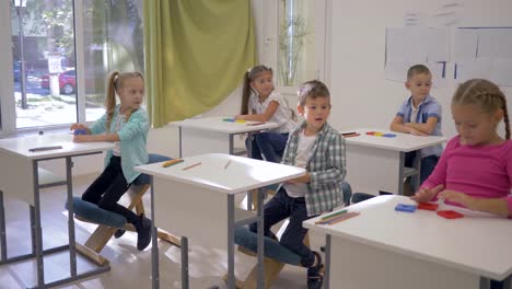 Kinder-in-der-Schule,-jungen-und-Mädchen-sitzen-am-Schreibtisch-und-heben-die-Hände-während-der-Lektion-im-Klassenzimmer-in-der-Schule