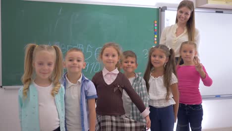 Grupo-de-niños-de-escuela-primaria-con-joven-educador-están-sonriendo-y-mira-la-cámara-sobre-fondo-de-pizarra