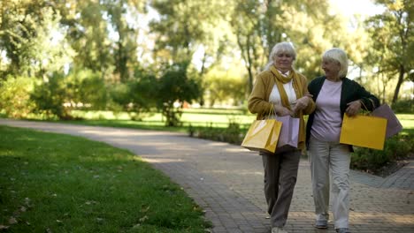 Elder-women-walking-in-park,-showing-and-boasting-purchases-they-buy-in-shop