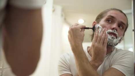 Man-Shaving-Beard-With-Razor-In-Bathroom