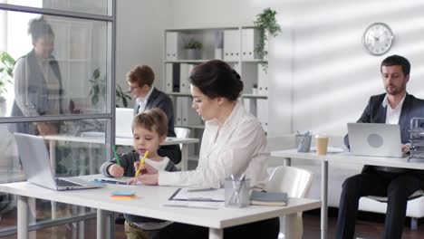 Mujer-empresaria-trabajando-en-el-escritorio-mientras-que-el-niño-dibujo-con-lápices