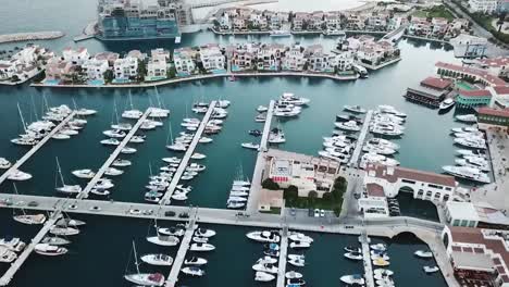 die-Drohne-fliegt-über-die-Marina-in-Limassol,-weiße-Yachten-und-Häuser-auf-dem-Hintergrund-von-türkisfarbenem-Wasser