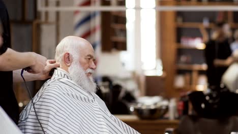 Professional-stylist-makes-modern-hairstyle-to-old-man-in-barbershop