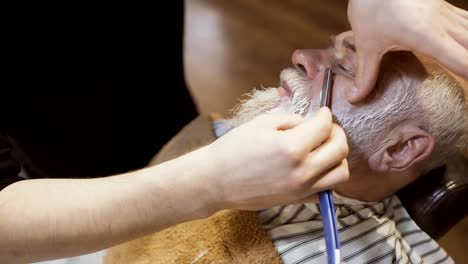 Barbier-rasiert-Gesicht-eines-älteren-Mannes-mit-Klinge-und-Sahne