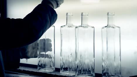 A-plant-worker-looks-at-bottles-on-a-light-background-and-checks-the-necks.-4K.