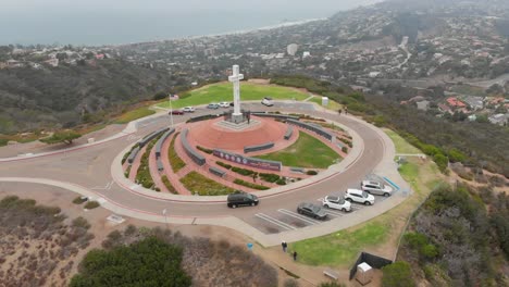 MT.-Soledad-Drone-volando-lentamente-sobre-el-monumento-de-la-Cruz-en-San-Diego,-California-con-coches,-árboles,-hierba-y-a-la-vista-de-la-costa