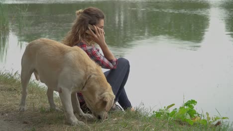 Mujer-rizada-y-labrador-está-descansando-cerca-del-río