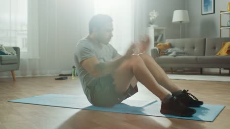 Starker-Athletic-Fit-Mann-in-T-shirt-und-Shorts-ist-tun-Abdominal-Crunch-Übungen-zu-Hause-in-seine-geräumige-und-helle-Wohnzimmer-mit-minimalistisches-Interieur.