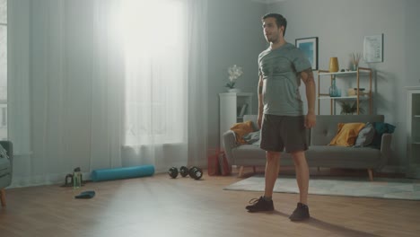 Athletic-Fit-hombre-en-camiseta-y-pantalones-cortos-es-haciendo-sentadilla-ejercicios-en-casa-en-su-amplio-y-luminoso-apartamento-con-Interior-minimalista.