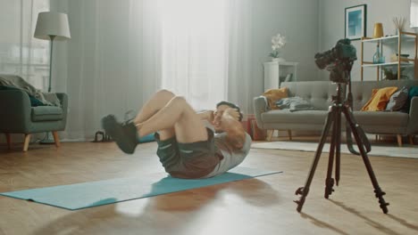 Strong-Athletic-Fit-Man-in-T-shirt-and-Shorts-is-Recording-his-Crisscross-Crunch-Workout-on-Camera-for-His-Blog.-Scene-takes-place-in-His-Spacious-and-Bright-Living-Room-with-Minimalistic-Interior.