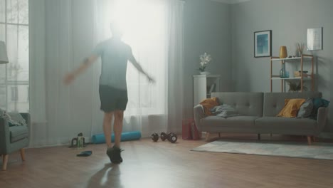 Strong-Athletic-Fit-Man-in-T-shirt-and-Shorts-is-Doing-Jumping-Jack-Exercises-at-Home-in-His-Spacious-and-Bright-Apartment-with-Minimalistic-Interior.