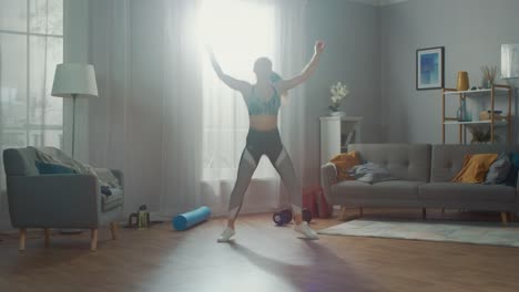 Strong-and-Beautiful-Fitness-Girl-in-an-Athletic-Top-is-Doing-Jumping-Jack-Exercises-in-Her-Bright-and-Spacious-Living-Room-with-Minimalistic-Interior.